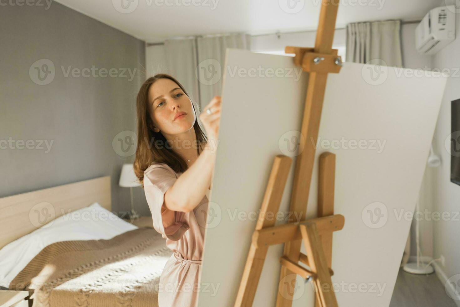 Young woman artist painting on canvas on the easel at home in bedroom - art and creativity concept photo