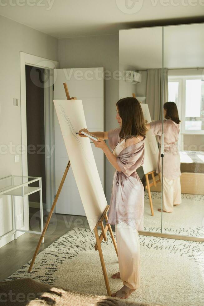 Young woman artist painting on canvas on the easel at home in bedroom - art and creativity concept photo