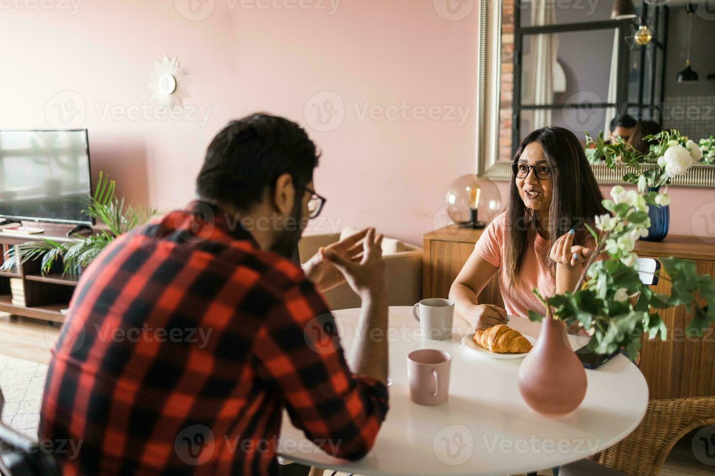 Happy couple eating breakfast and talking at dining table in morning. Indian girl and latino guy. Relationship and diversity concept photo