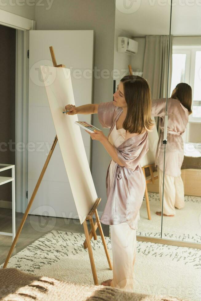 Young woman artist painting on canvas on the easel at home in bedroom - art and creativity concept photo