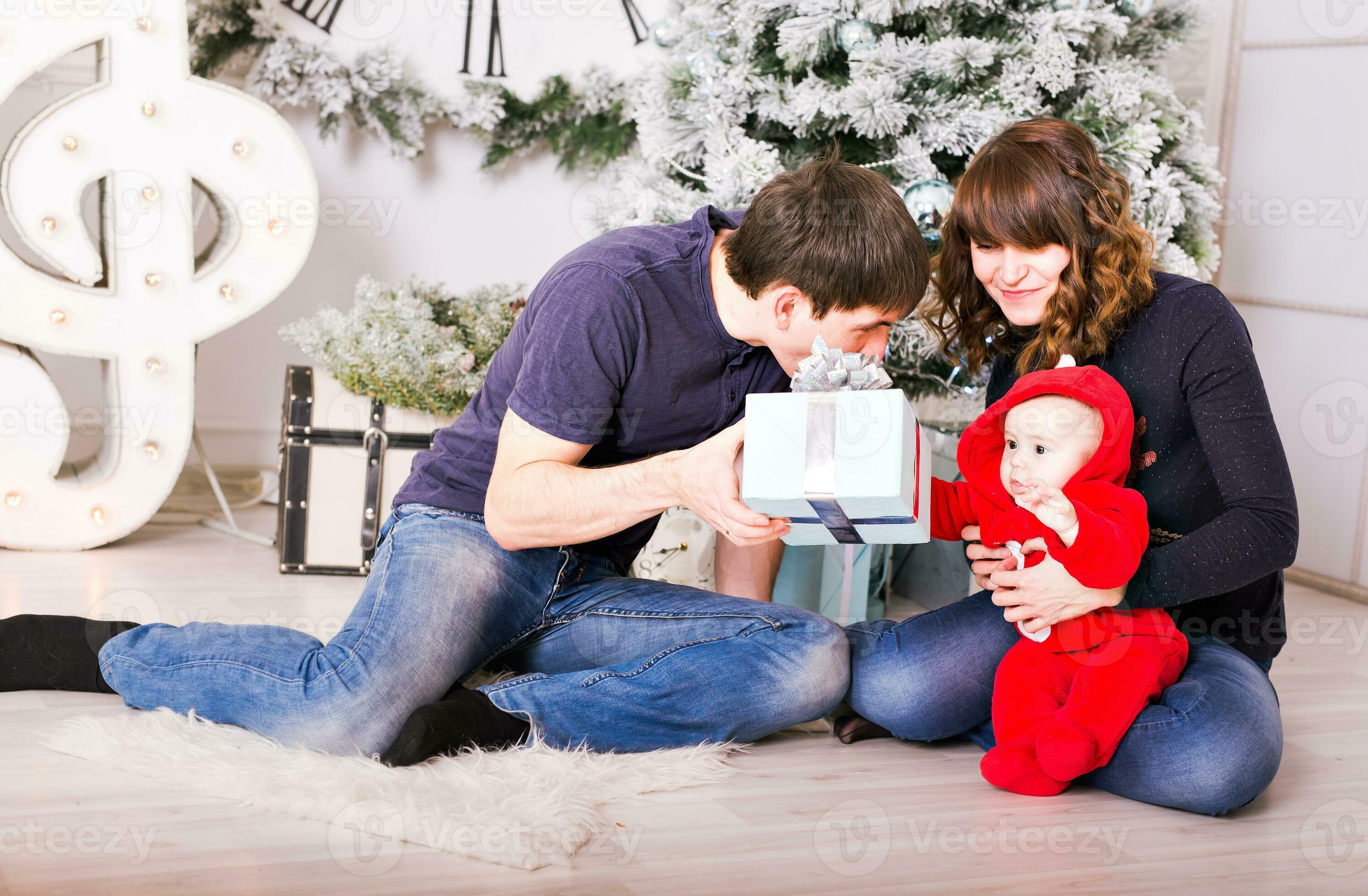 Christmas Family with baby opening gifts. Happy Smiling Parents and Child at Home Celebrating