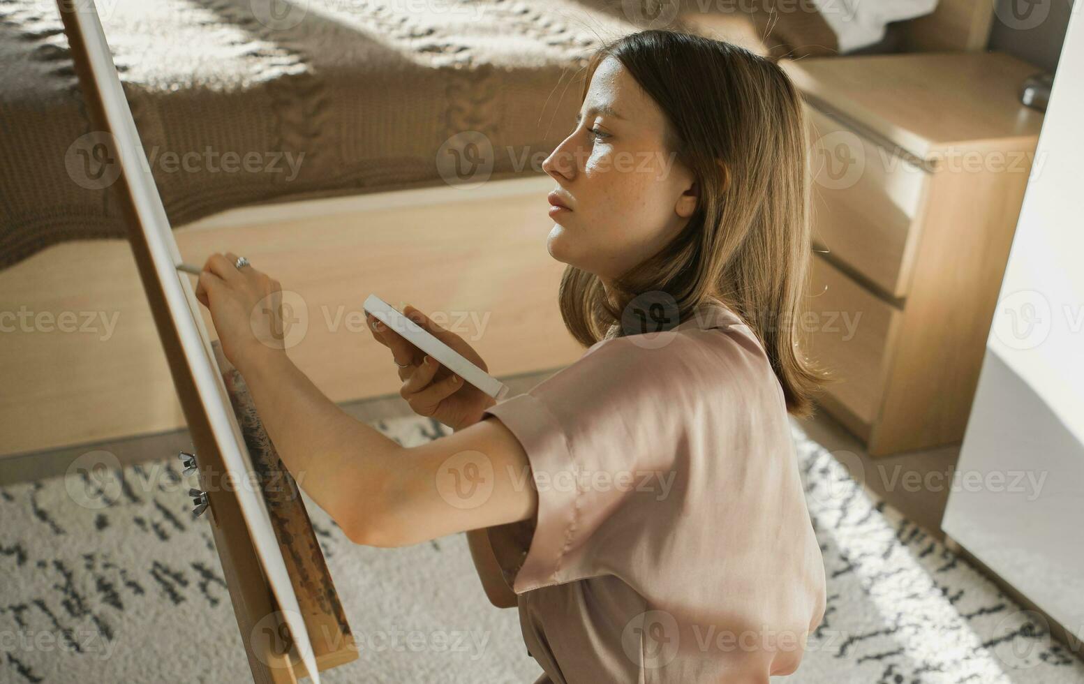 Young woman artist painting on canvas on the easel at home in bedroom - art and creativity concept photo