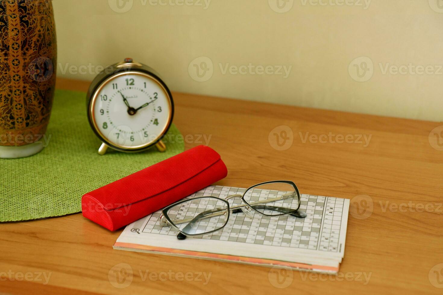 crosswords, a case with glasses, an alarm clock, a vase with a bouquet on the table, a pensioner's pastime photo