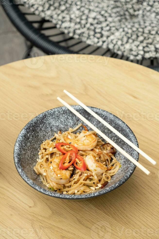 Udon noodles with shrimp and fried vegetables in a bowl top view on wooden table photo