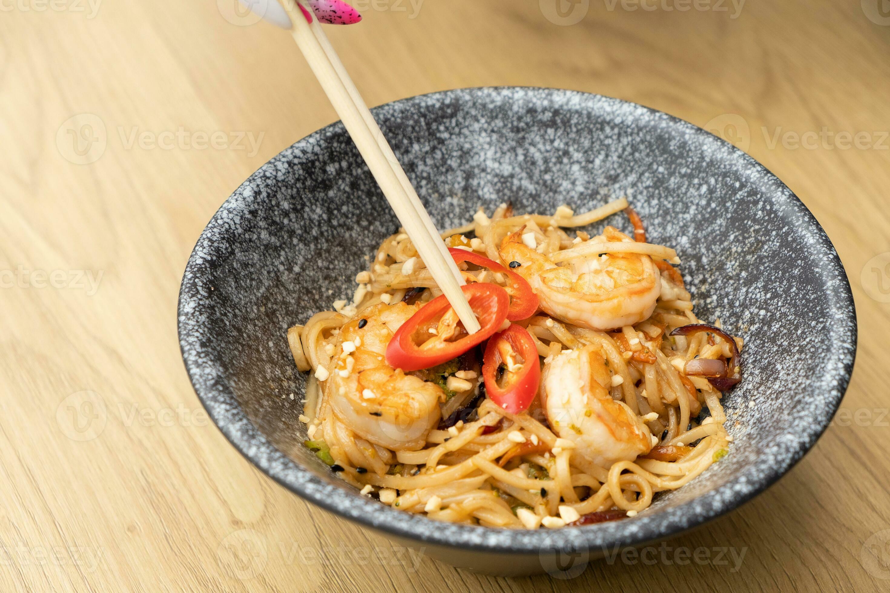 Udon noodles with shrimp and fried vegetables in a bowl top view