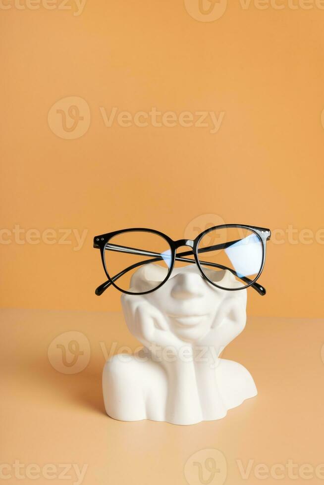 Gypsum head with eyeglasses on colored background. Optical store, vision test, stylish glasses concept photo