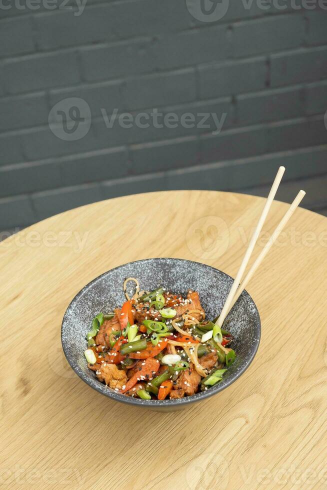 A bowl of udon noodles, veal and fried vegetables angle view on wooden table photo