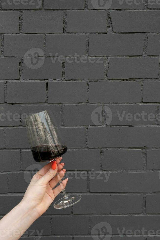 un vaso de rojo vino en un hembra mano en contra un oscuro gris ladrillo pared foto