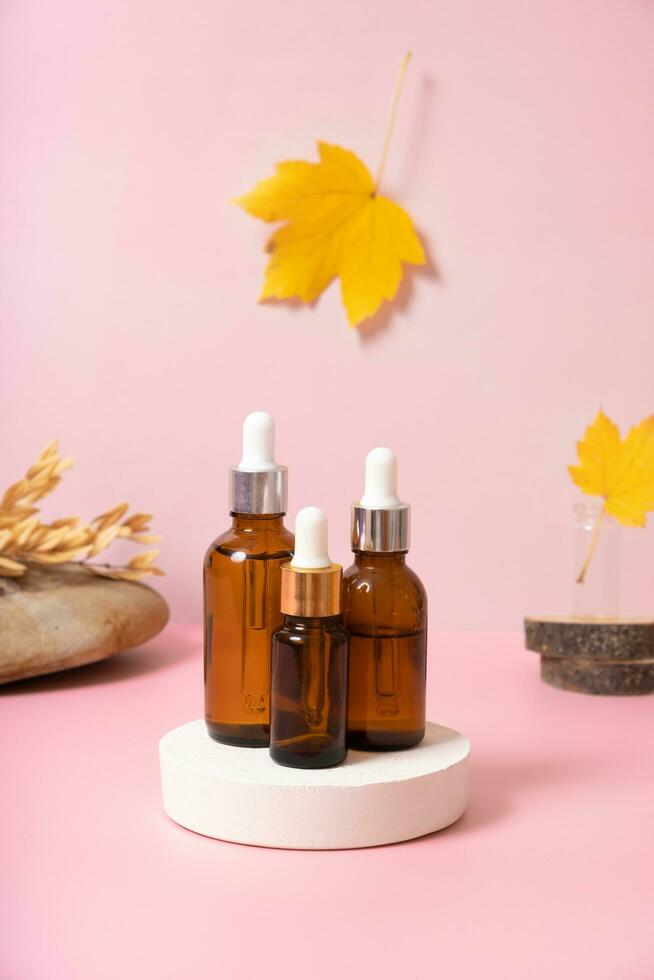 Glass dropper bottles with cosmetics oil or serum at autumn scene composition with podium photo