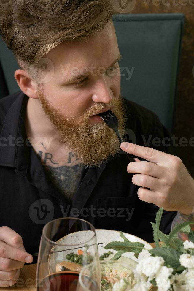 un joven hombre con un barba sabores comida a un restaurante mesa foto