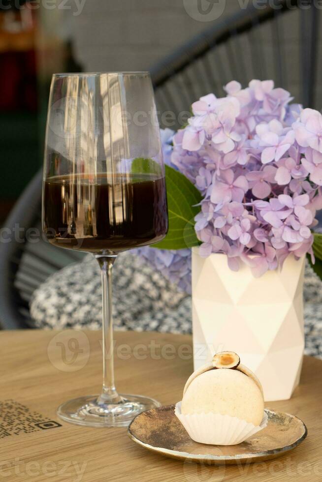 Macaroon anf coffee in wineglass on a wooden cafe table on flowers background photo