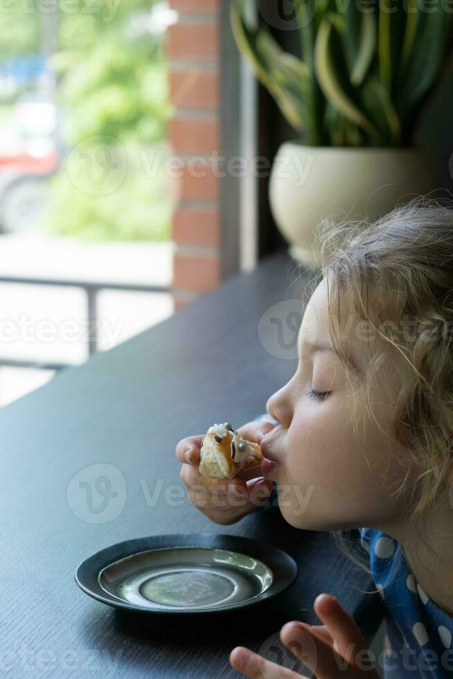 un pequeño niña felizmente come un rosquilla en un café foto