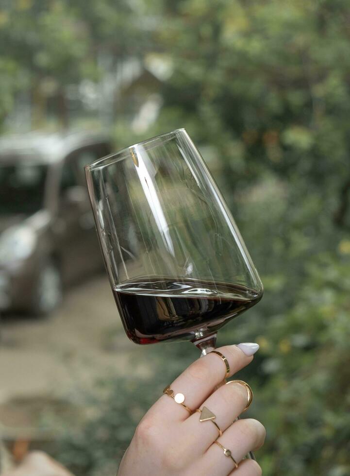 un vaso de rojo vino en un hembra mano en verdor antecedentes foto