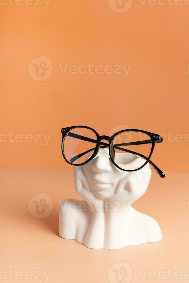 Gypsum head with eyeglasses on colored background. Optical store, vision test, stylish glasses concept photo