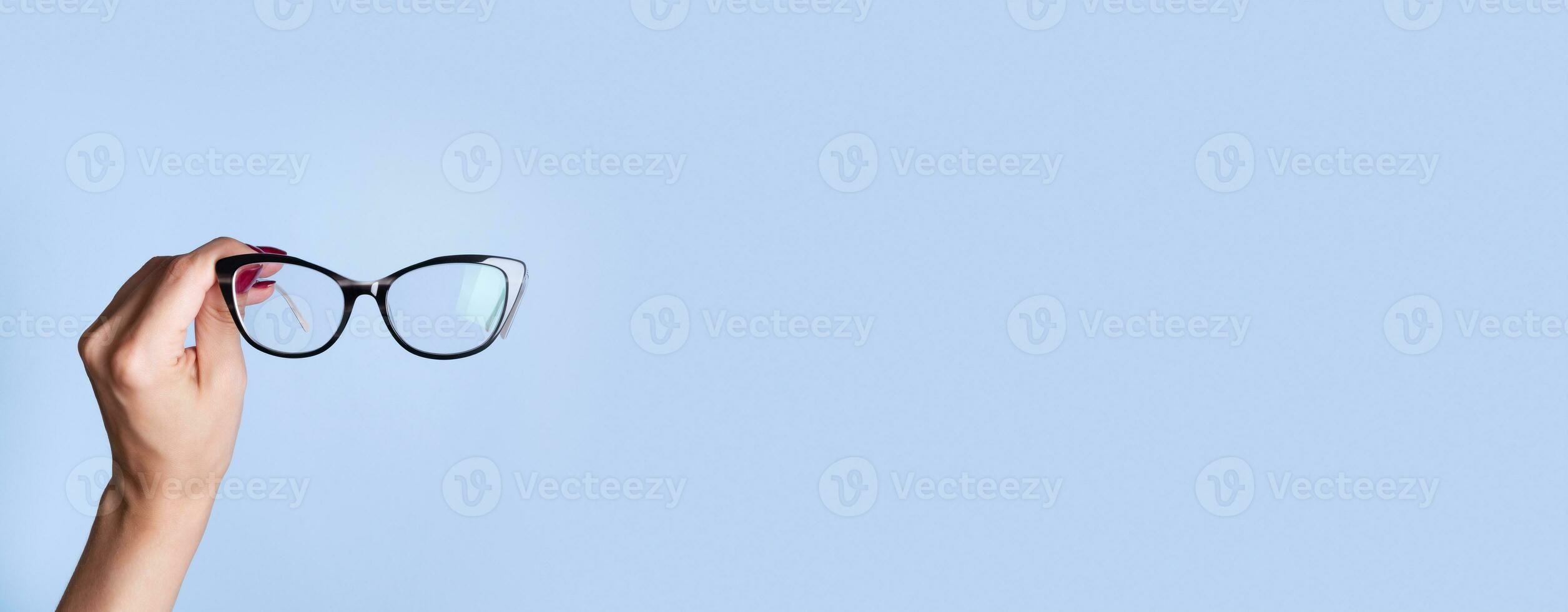 Stylish eyeglasses in female hand on blue banner background. Optical store, vision test concept. Banner format. photo