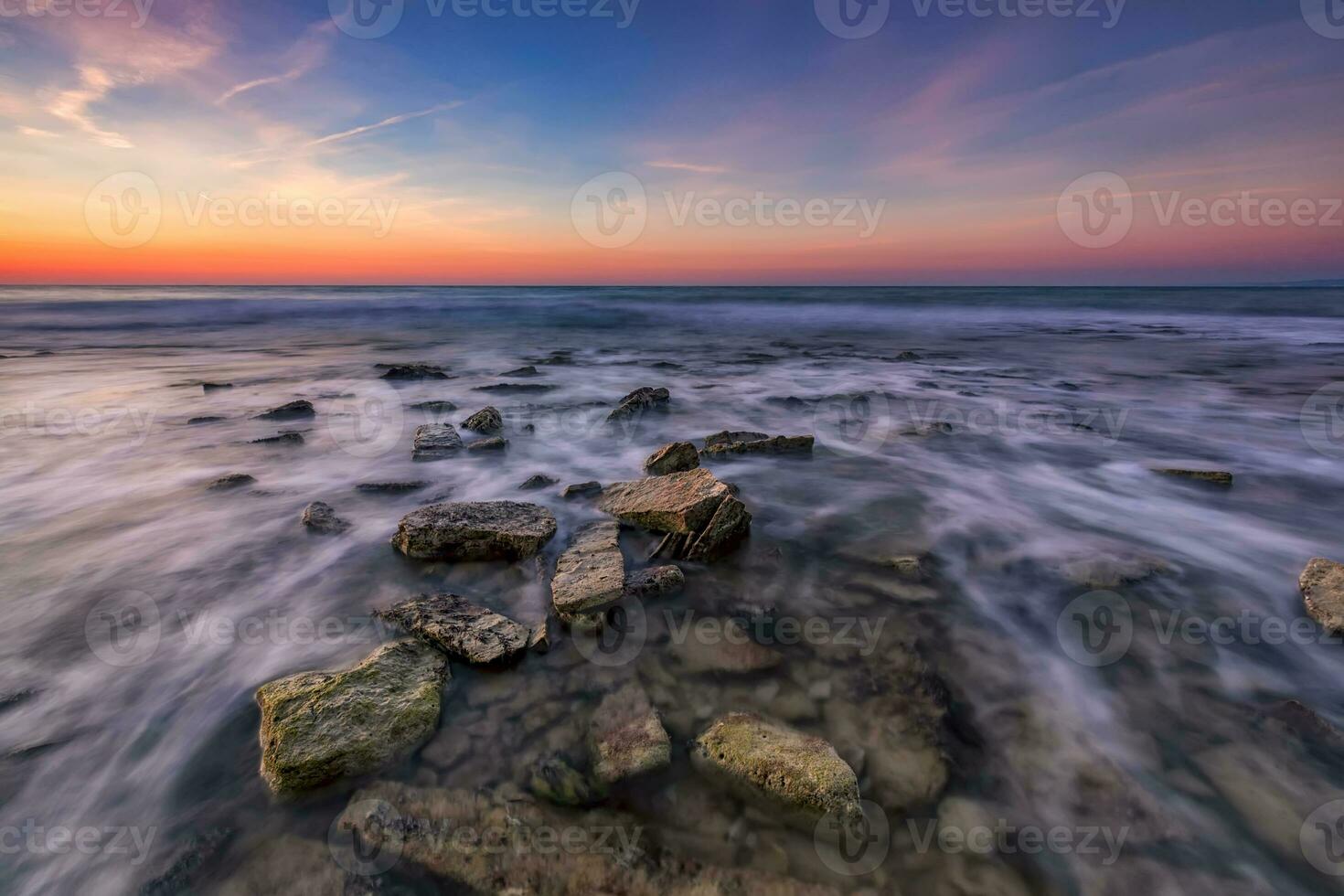 Beautiful rocky beach with stones in blurred water, the colorful sky at sunrise. Black sea, Bulgaria. Landscape with the sea waves and rocks. photo