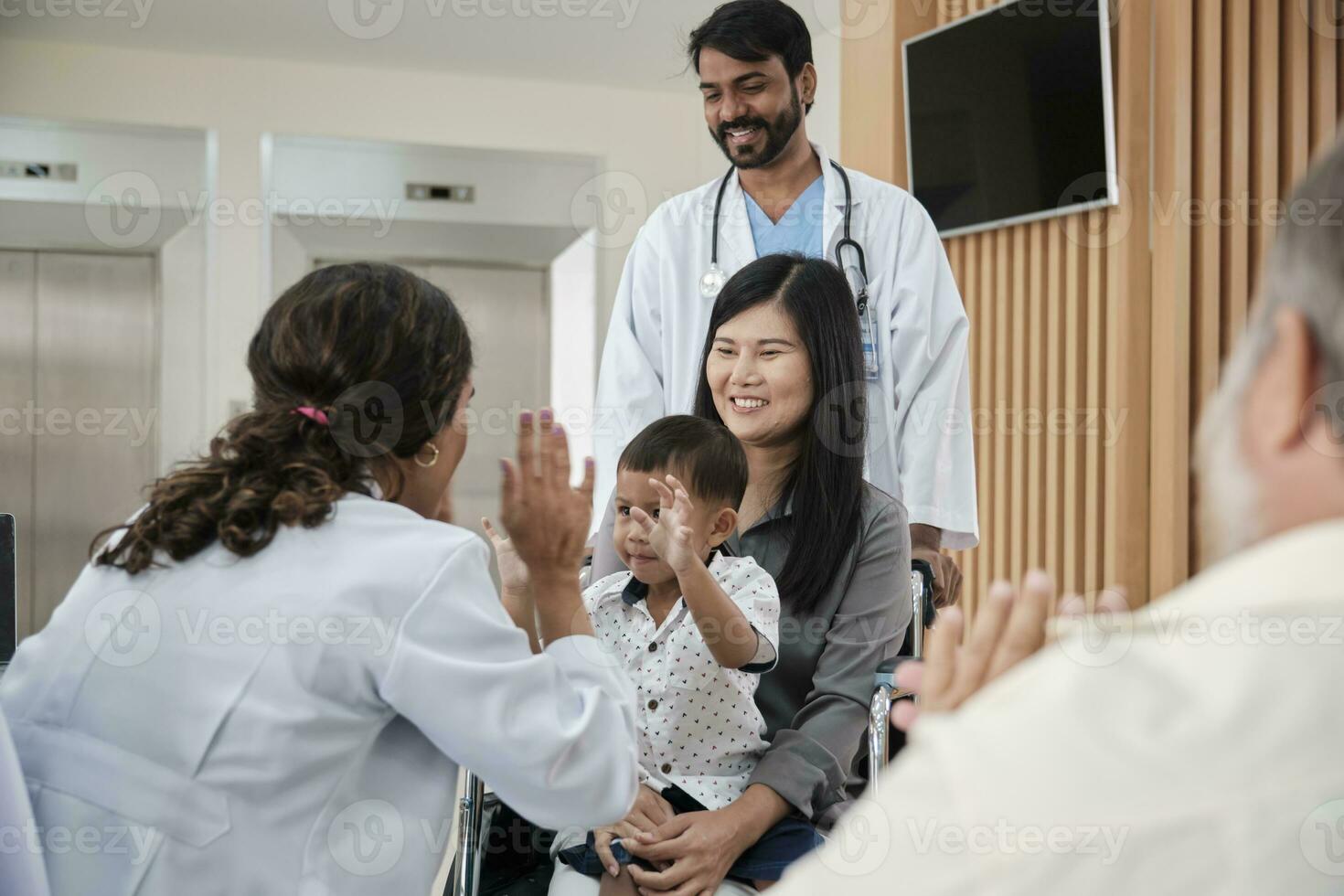 Happy young female pediatric doctor in uniform teasing little boy in wheelchair for medical exam at outpatient clinic hospital, people public health care checkup, and appointment visit. photo