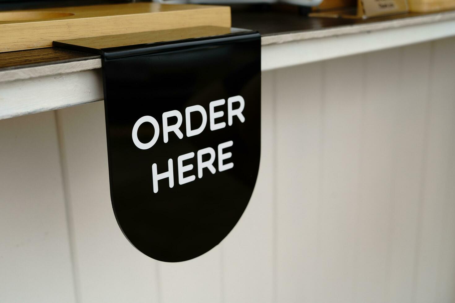 The order here sign in white letters on a black plastic sheet hanging at the coffee shop bar counter photo