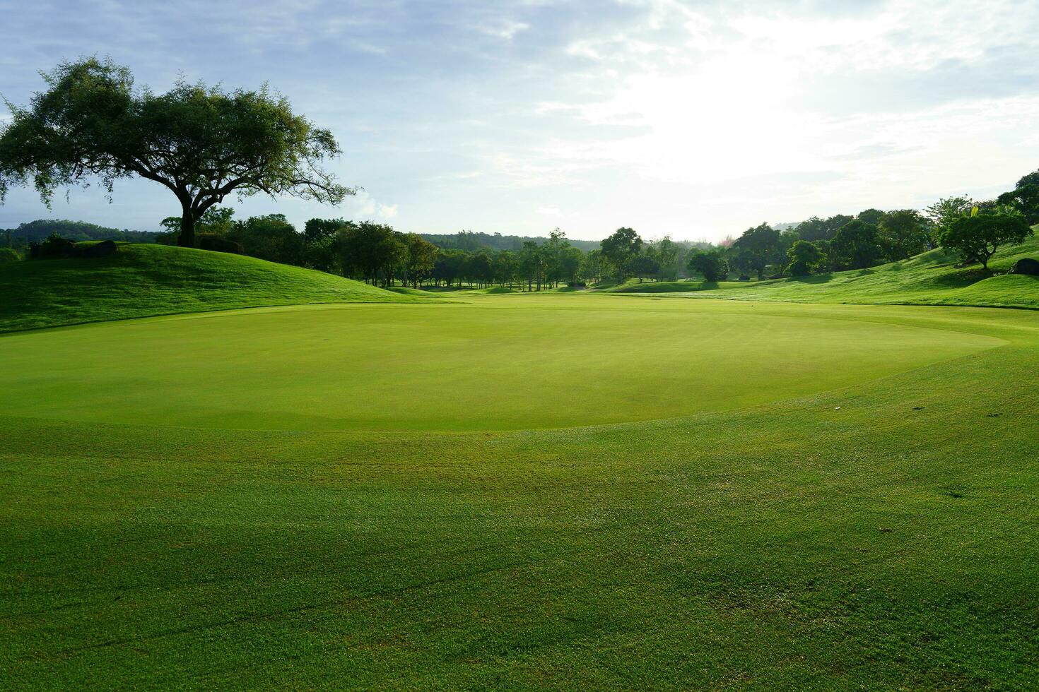 Golf green in the morning sun backlit against cloudy sky photo