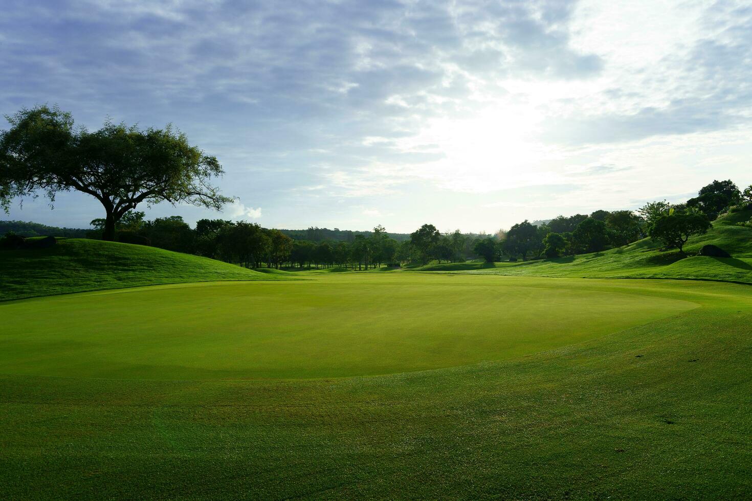 Golf green in the morning sun backlit against cloudy sky photo