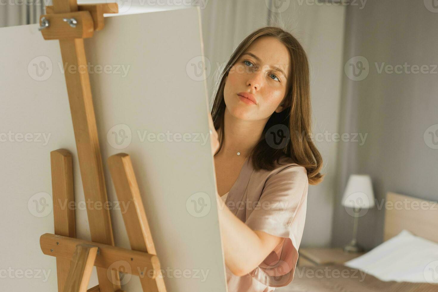 Young close-up woman artist painting on canvas on the easel at home in bedroom - art and creativity concept photo