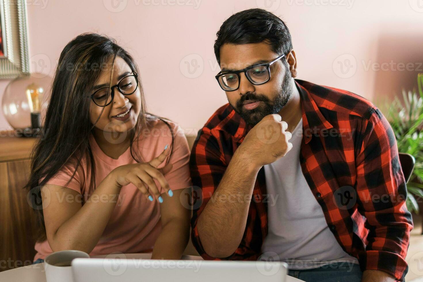 Indian family couple cuddle at desk make video call to friends using laptop webcam. Loving young spouses look at computer screen waving hands in good mood greeting parents communicating online via app photo