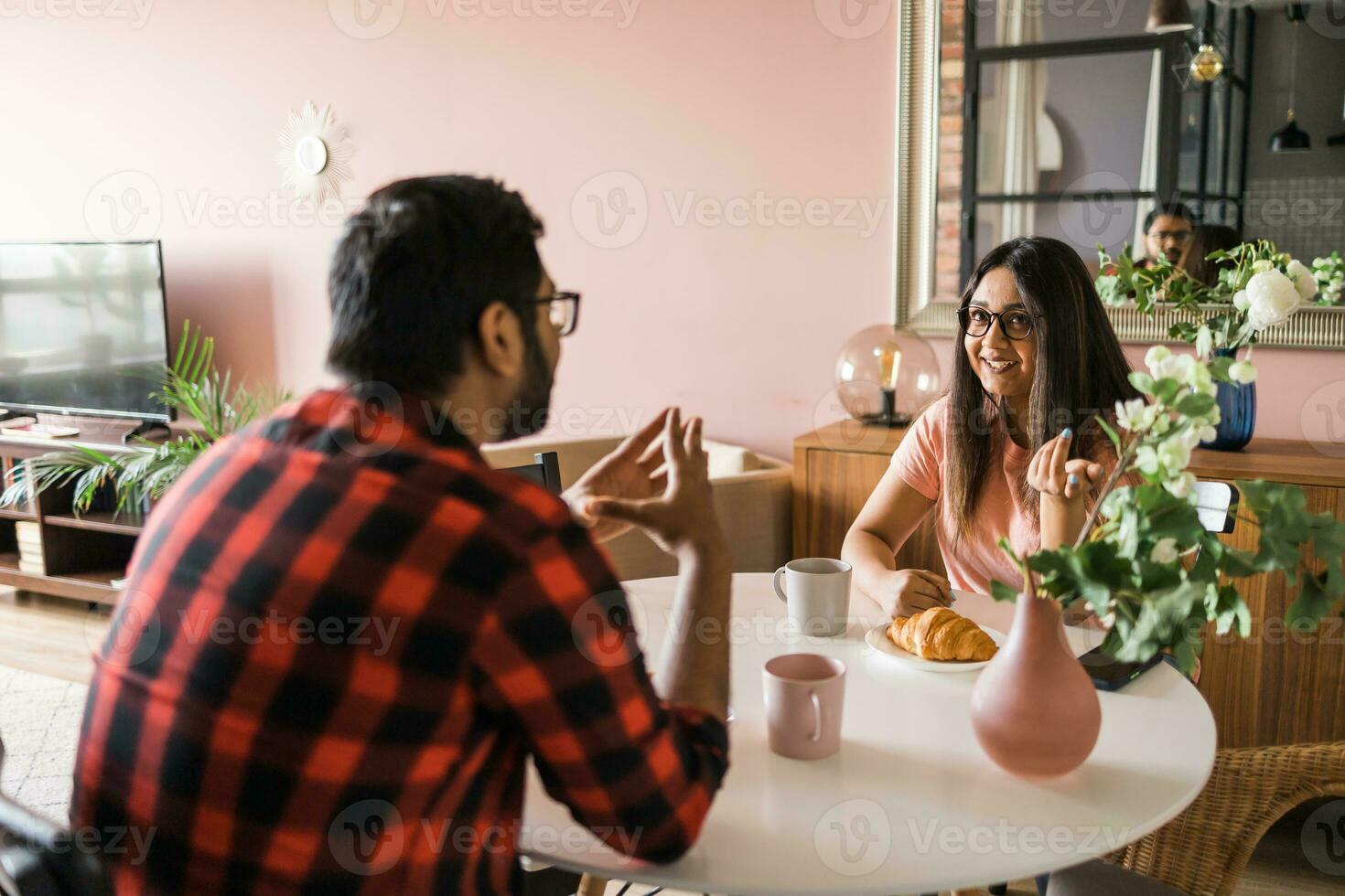 Happy indian couple having breakfast and small talk together in the kitchen - friendship, dating and family photo