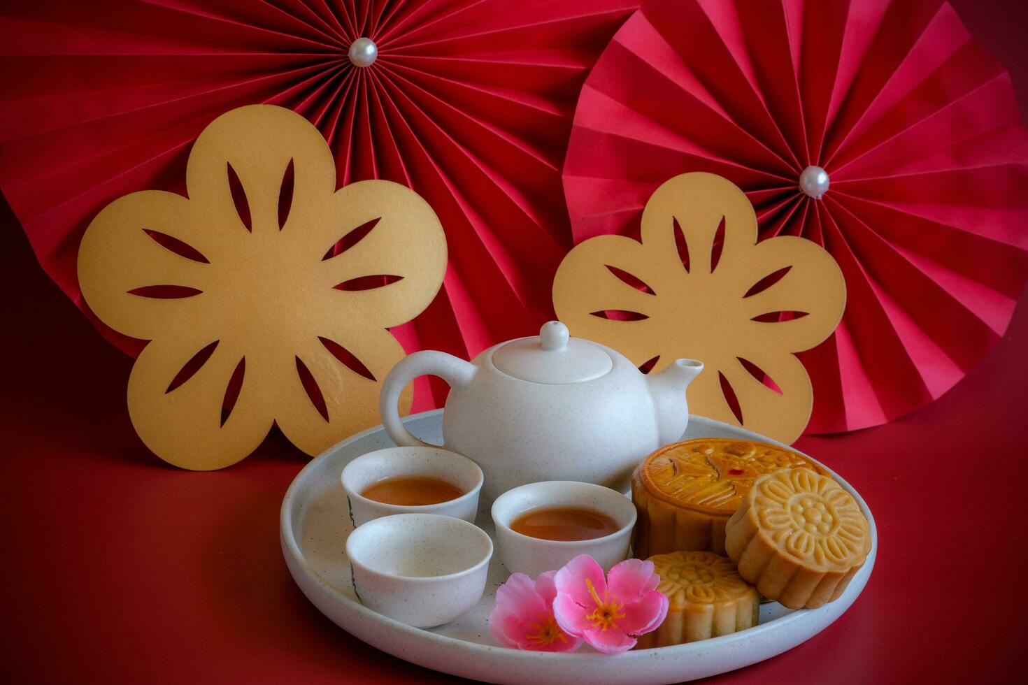 Chinese Mid-Autumn Festival concept made from mooncakes, tea decorated with plum blossom, rabbit and red paper fans on red background. photo