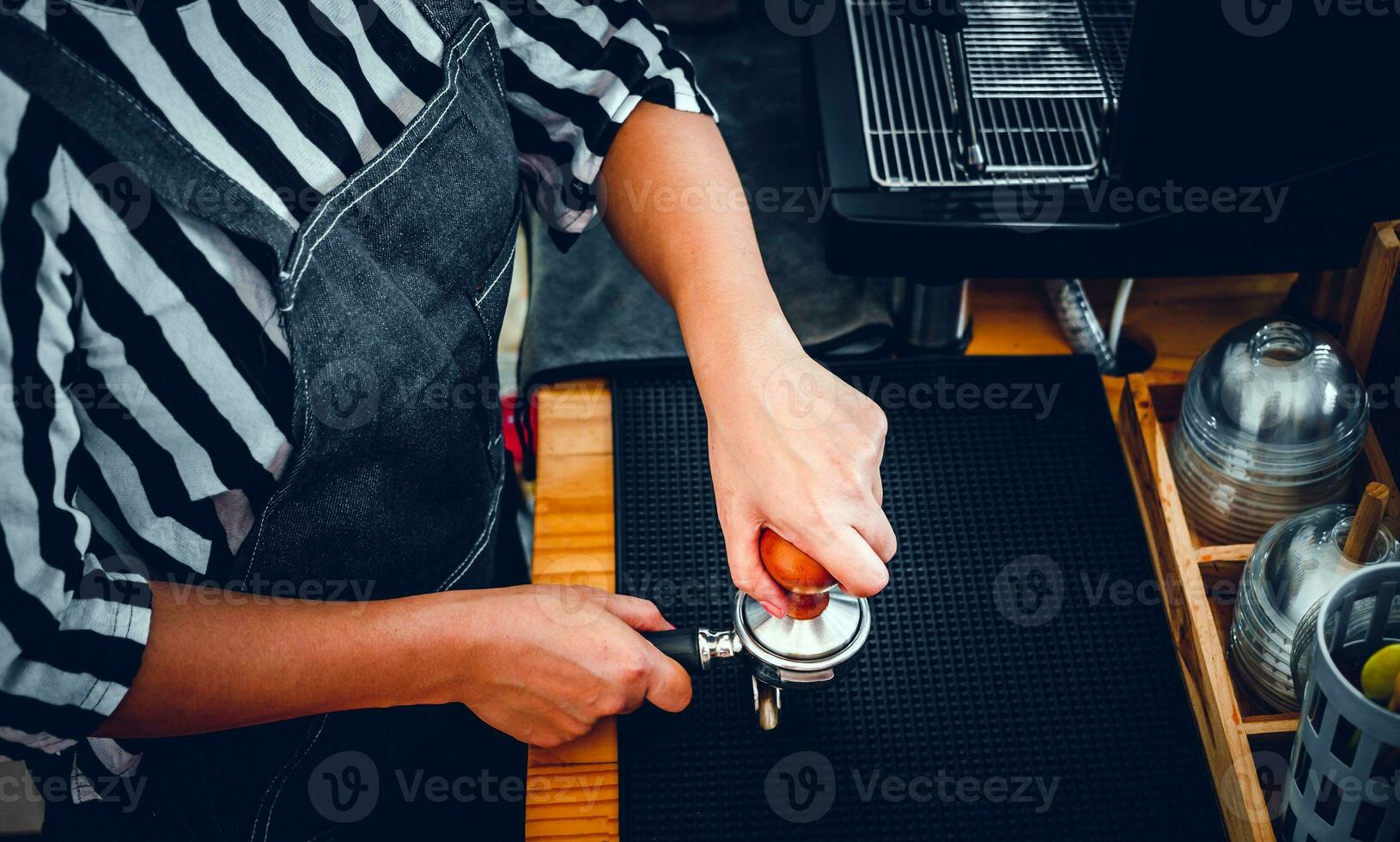 Barista holding portafilter and coffee tamper making an espresso coffee in cafe photo
