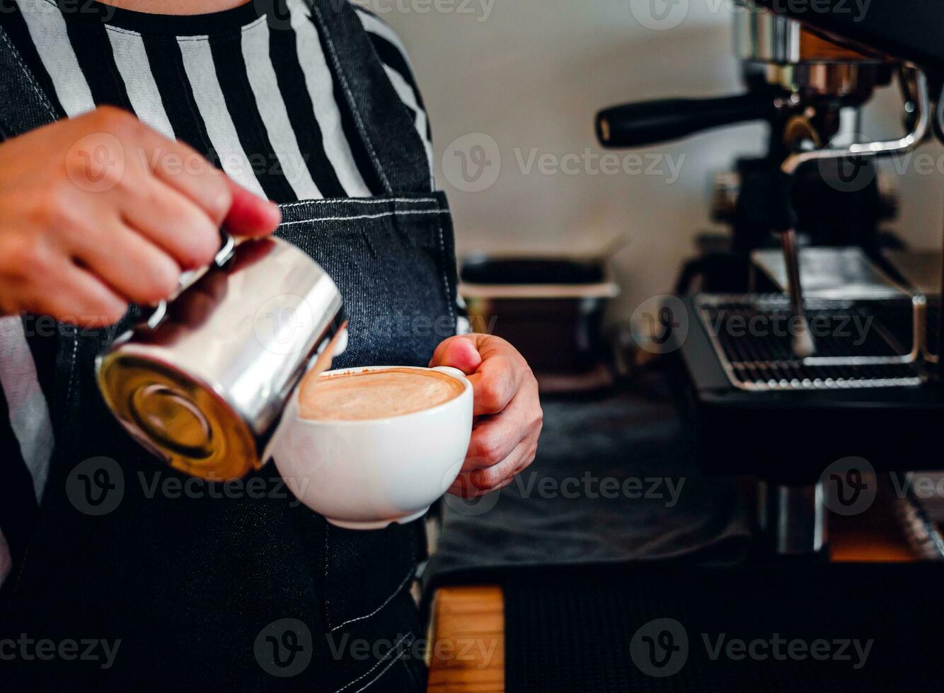 Close-up of the hand of a professional barista in a coffee shop making  pouring steamed milk into the coffee cup making cappuccino menu photo