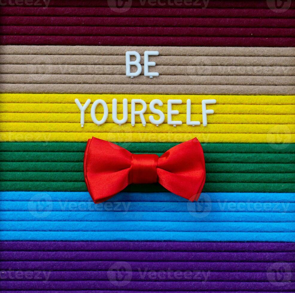 a red bow tie sits on a rainbow striped background with words Be yourself photo