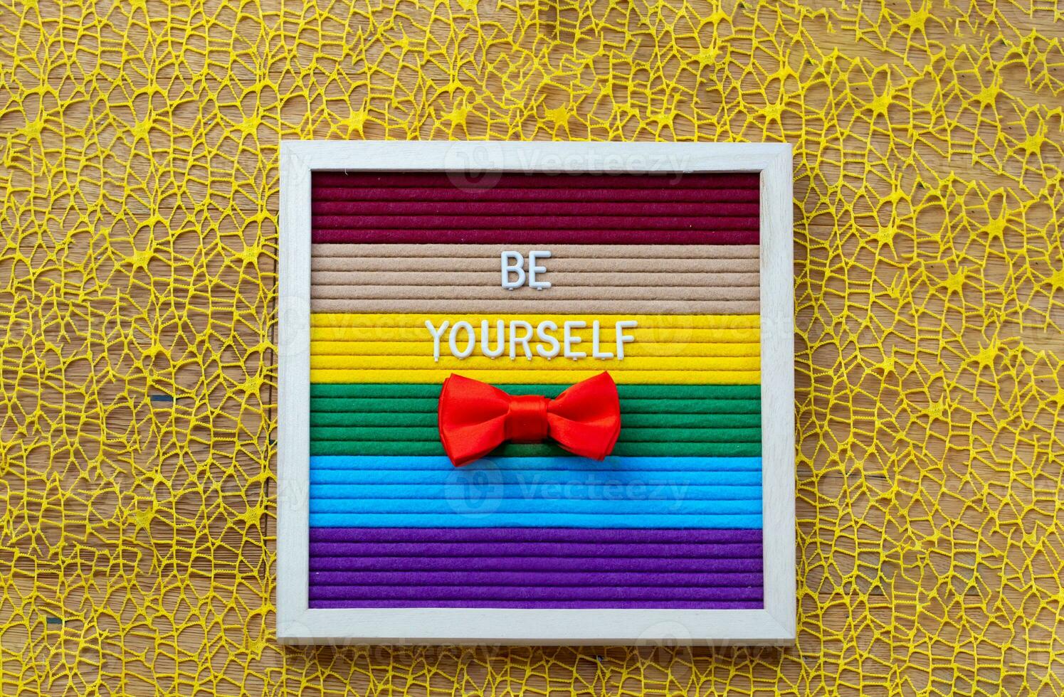 a red bow tie sits on a rainbow striped background with words Be yourself photo