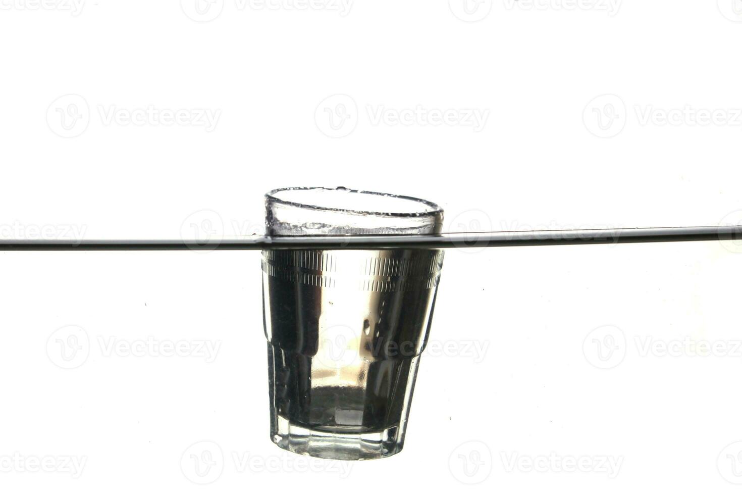 A glass of water immersed in water floats on a white background. photo