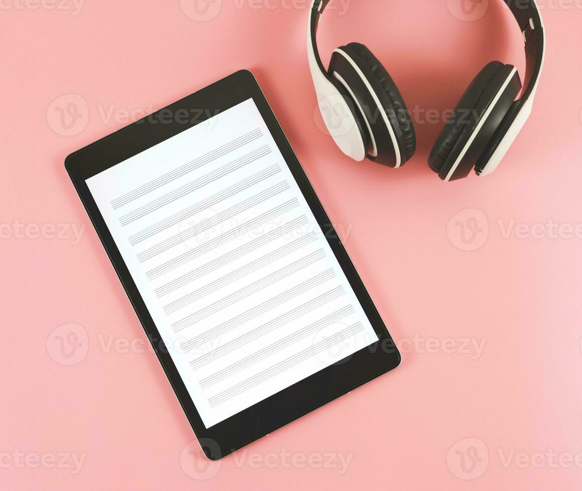 flat lay of digital tablet with music staff  screen and white headphones on pink background. music composer on digital tablet. photo