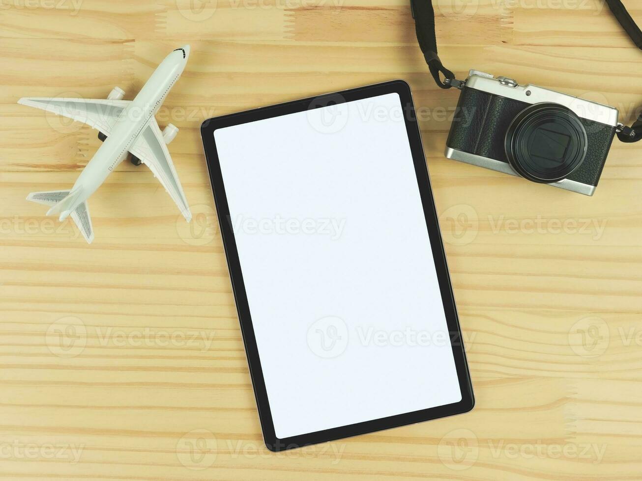 flat lay of digital tablet with blank white screen, airplane model and digital camera isolated on wooden table  background. travel planning concept. photo