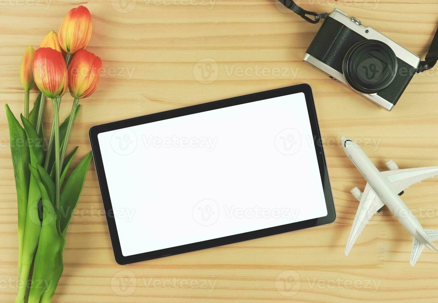 plano laico de digital tableta con blanco blanco pantalla, tulipán flores, avión modelo y digital cámara aislado en de madera mesa antecedentes. foto