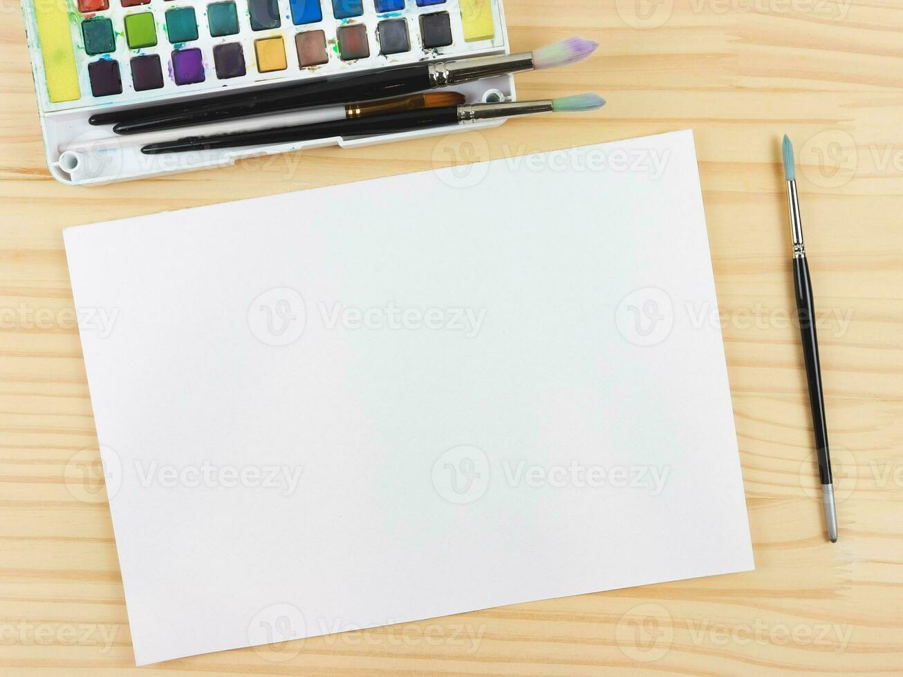 flat lay of artist workspace. Blank paper, Drawing tools, stationary supplies, Watercolor paints and brushes and paper on wooden table, copy space. photo