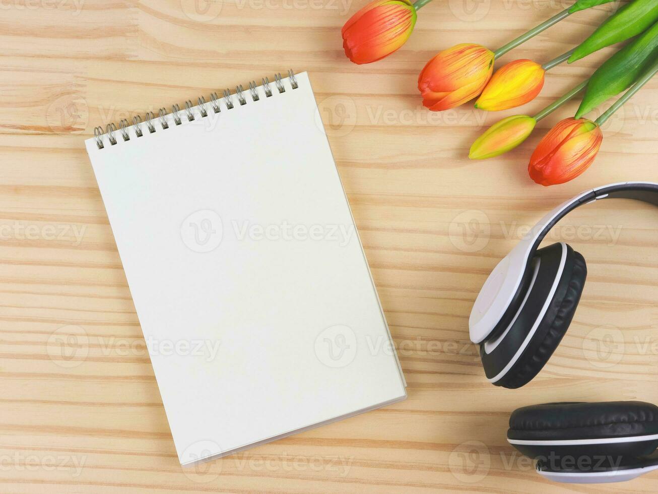 open empty page notebook, white headphones and red yellow tulip flowers on wooden table background with copy space. Love song, spring music, podcast and Audio book. photo