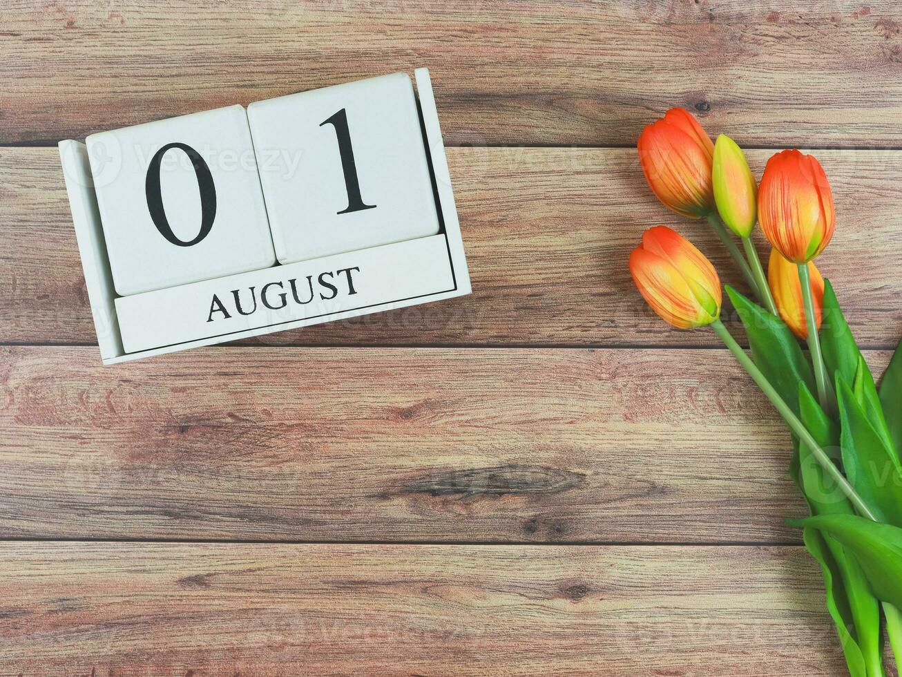 flat lay of wooden calendar with date August 01 on wooden table background with orange and yellow tulips, copy space. photo