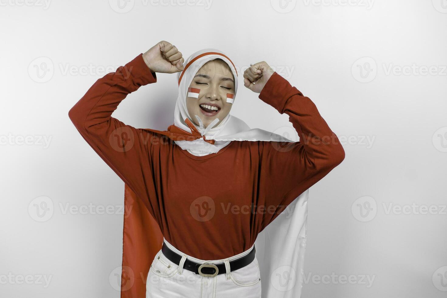 A young Asian muslim woman with a happy successful expression wearing red top and white hijab while holding Indonesia's flag, isolated by white background. Indonesia's independence day concept. photo