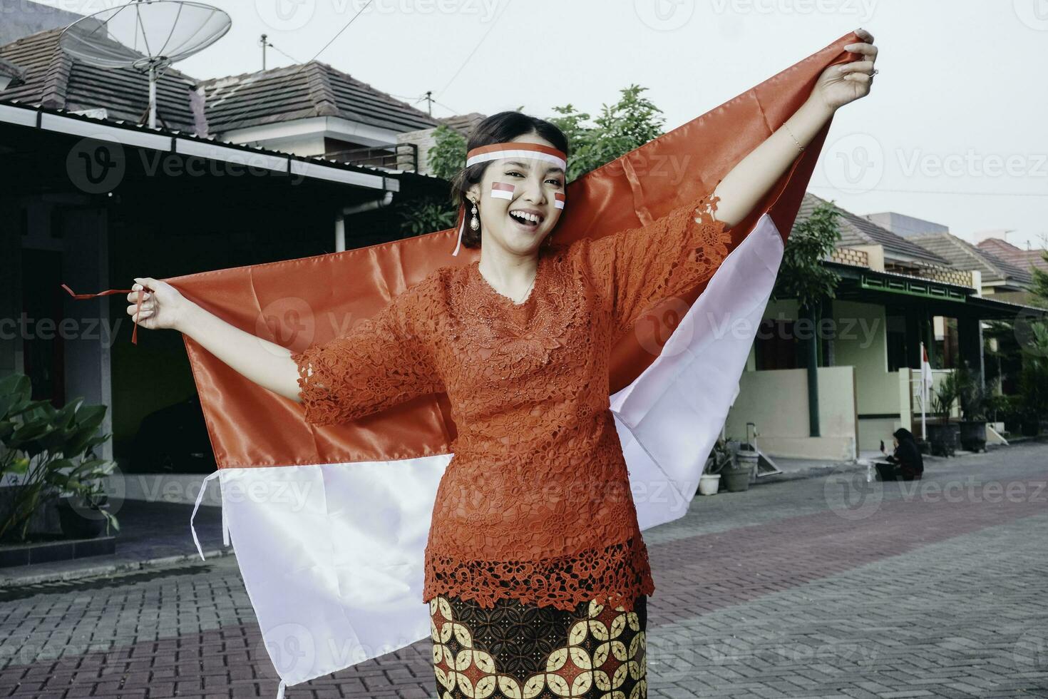 Happy smiling Indonesian woman wearing red kebaya holding Indonesia's flag to celebrate Indonesia Independence Day. Outdoor photoshoot concept photo
