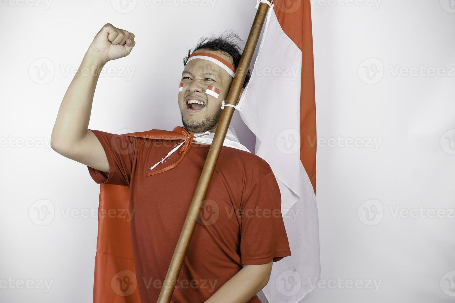 A young Asian man with a happy successful expression wearing red top and headband while holding Indonesia's flag, isolated by white background. Indonesia's independence day concept. photo