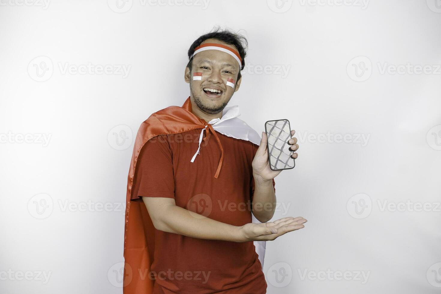 un retrato de un sonriente asiático hombre vistiendo venda y demostración su teléfono, aislado por blanco antecedentes. de indonesia independencia día concepto foto
