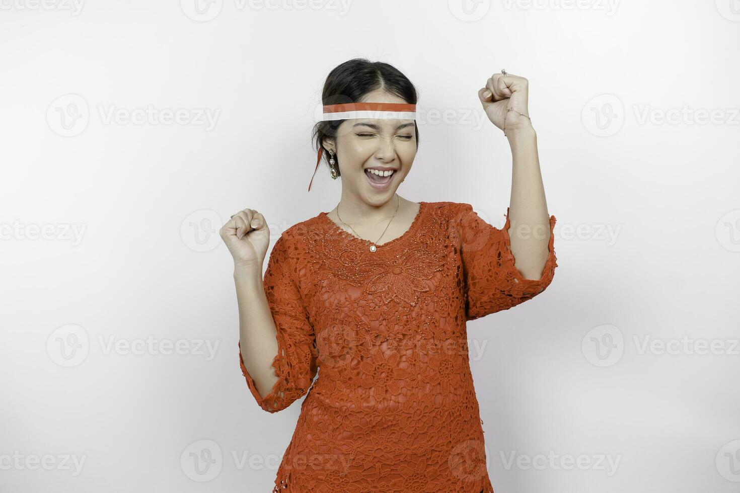 A young Asian woman with a happy successful expression wearing red kebaya and headband isolated by white background. Indonesia's independence day concept. photo