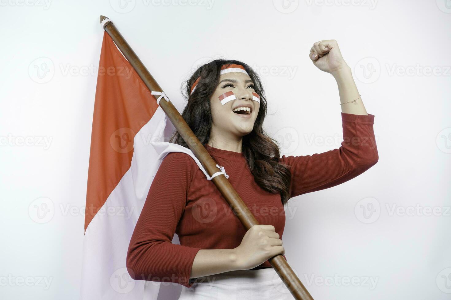 A young Asian woman with a happy successful expression wearing red top and headband while holding Indonesia's flag, isolated by white background. Indonesia's independence day concept. photo