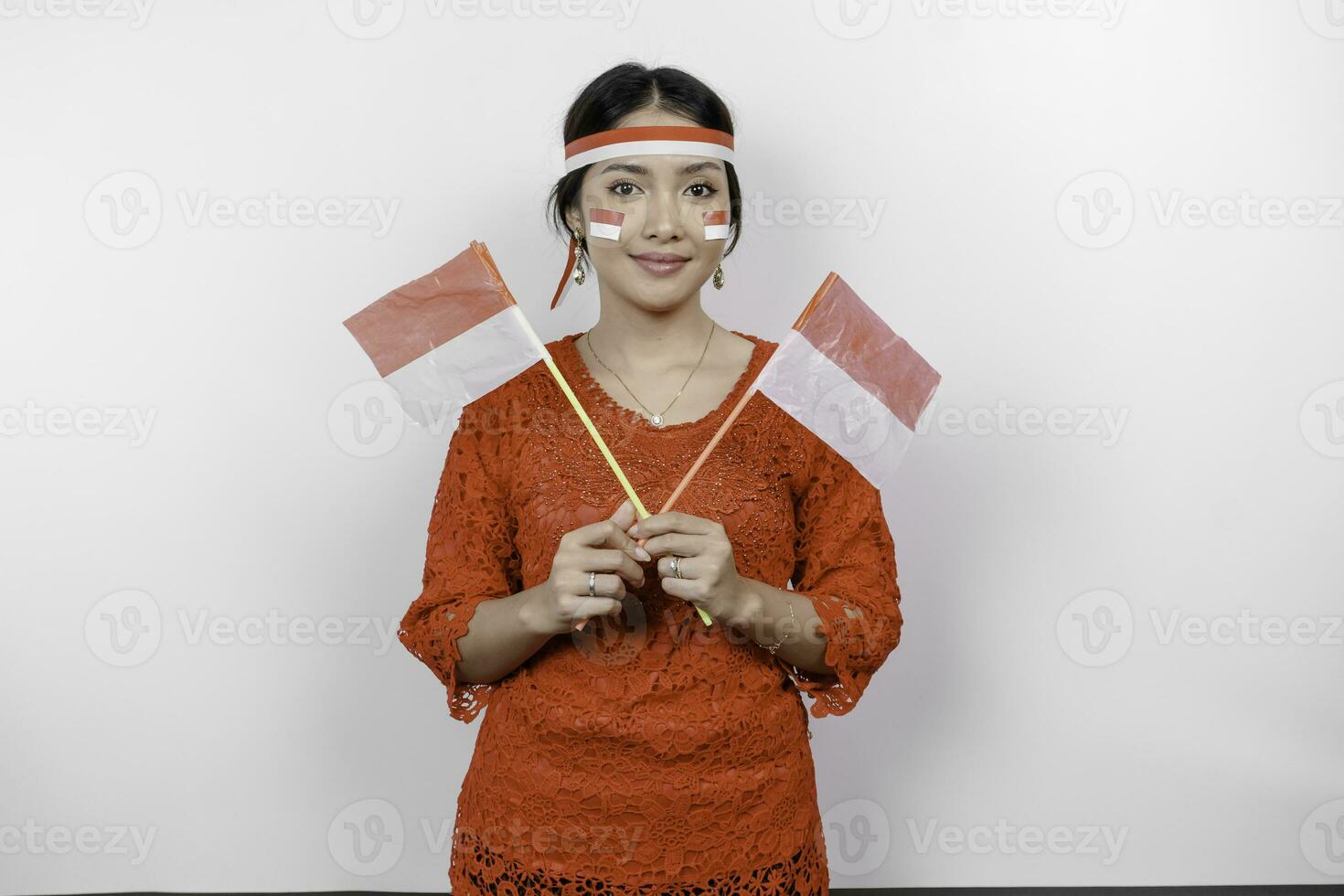 Happy smiling Indonesian woman wearing red kebaya and headband holding Indonesia's flag to celebrate Indonesia Independence Day isolated over white background. photo