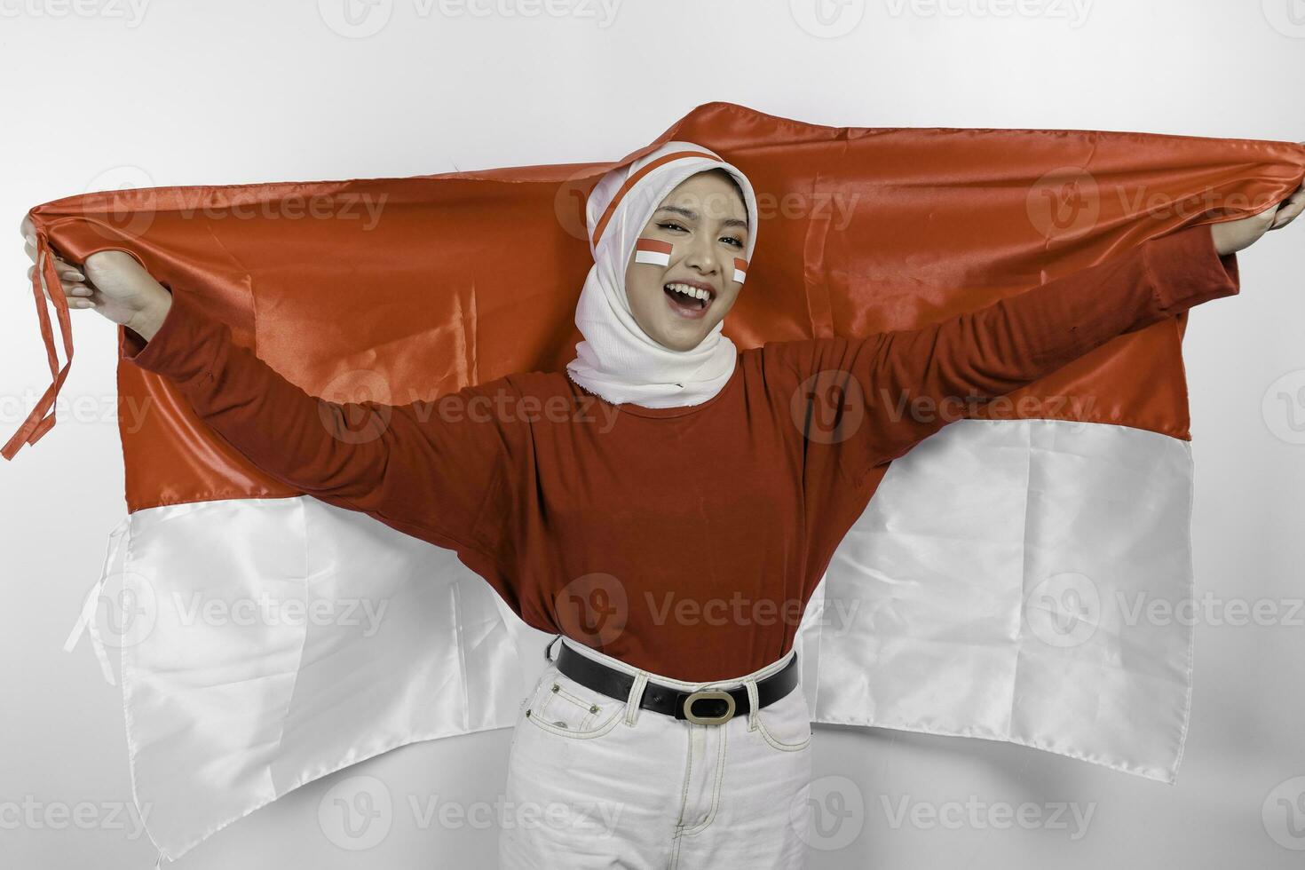 Happy smiling Indonesian muslim woman wearing red top and white hijab holding Indonesia's flag to celebrate Indonesia Independence Day. Isolated by white background. photo