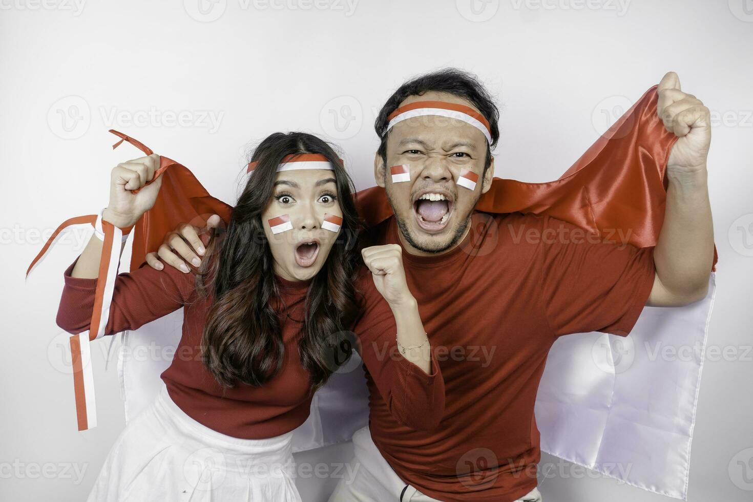 A young Asian couple with a happy successful expression wearing red top and headband while holding Indonesia's flag, isolated by white background. Indonesia's independence day concept. photo