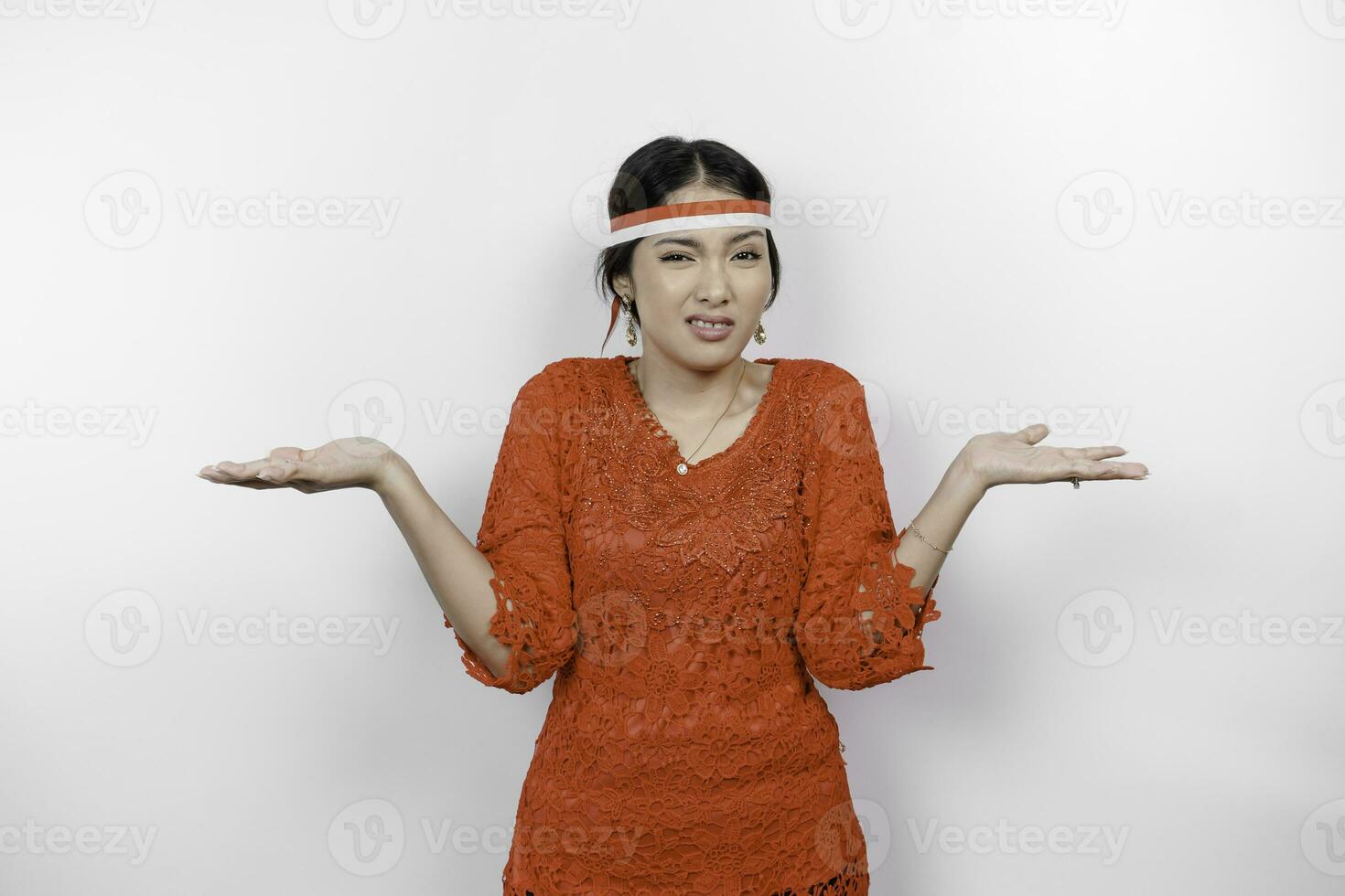 A thoughtful young woman wearing headband and red kebaya is looking aside confuse between choices, isolated by white background. Indonesia's independence day. photo
