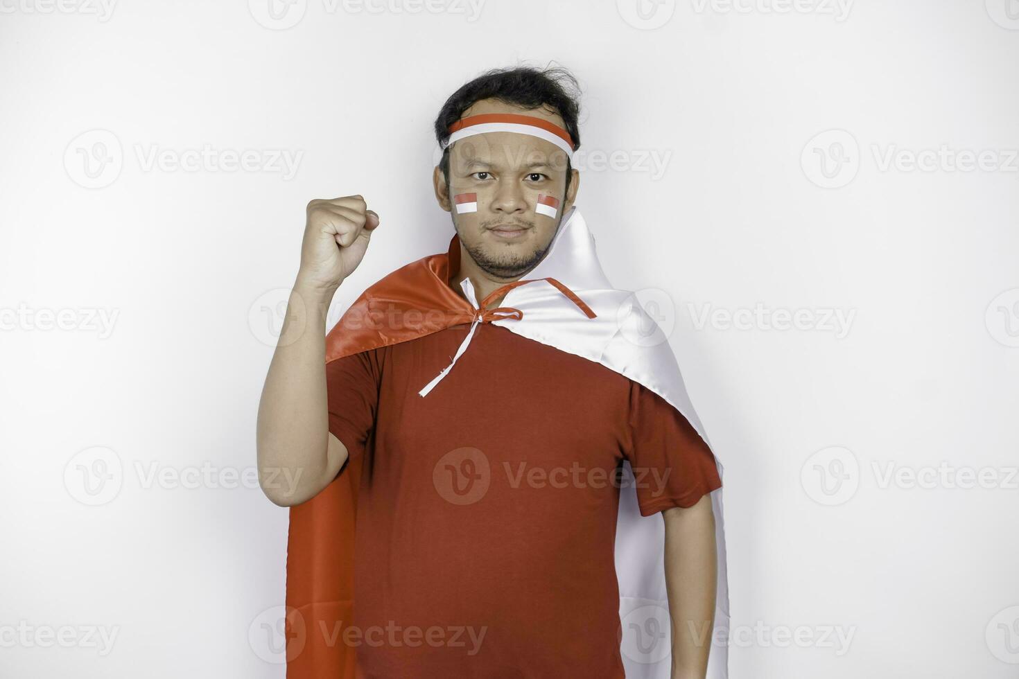 A young Asian man with a happy successful expression wearing red top and headband while holding Indonesia's flag, isolated by white background. Indonesia's independence day concept. photo